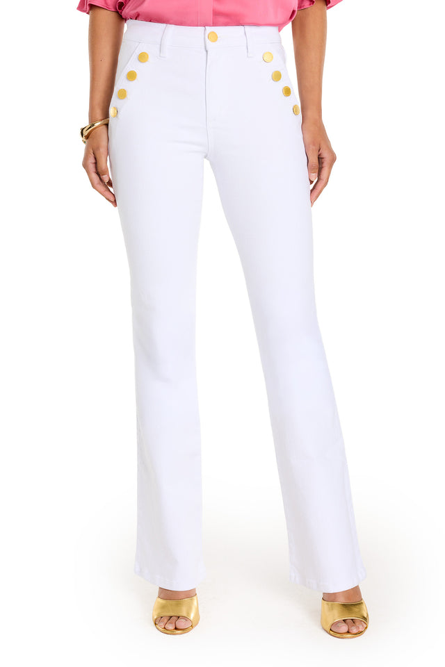 A person showcases the Allegra Bootcut Jean - White, featuring high-waisted, white bootcut denim with two rows of large gold buttons, paired with a pink blouse and yellow open-toe heels. Gold detailing adds a chic touch. Shown mid-torso to feet on white background.