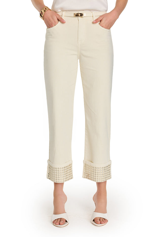 Wearing the Ren Cropped Cuff Jean - Gold Mirror, featuring cream color and wide, embellished cropped cuffs, paired with a slim belt, white heeled sandals, and a gold bracelet against a white background.