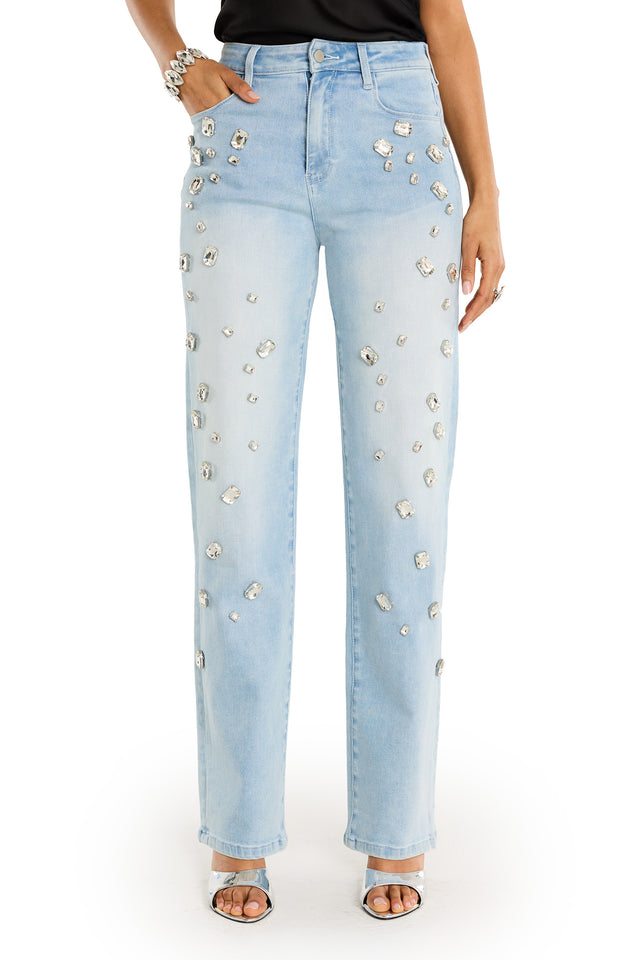A person wears the Tara Crystal Jean - Light Blue, a high-rise stretch denim jean embellished with sparkling rhinestones, paired with open-toe heels and a black top. Only the lower half of the body is visible.