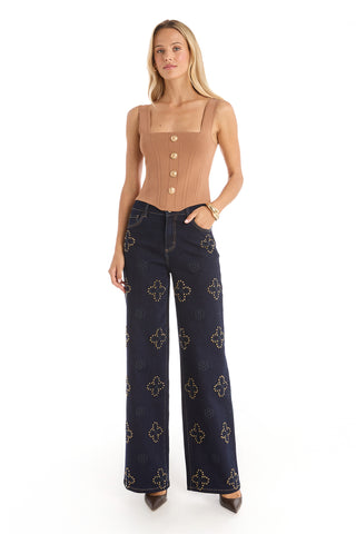 A woman with long blonde hair poses against a white background in the Venus Button Top - Mocha Mousse, a tan corset-inspired style with large buttons, paired with high-waisted wide-leg dark blue jeans with gold accents and brown heels.