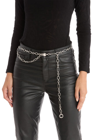A person wearing a black long-sleeve top, black leather pants, and the Arden Chain Belt - Silver with a circular charm, standing with one hand by their side and the other slightly bent.