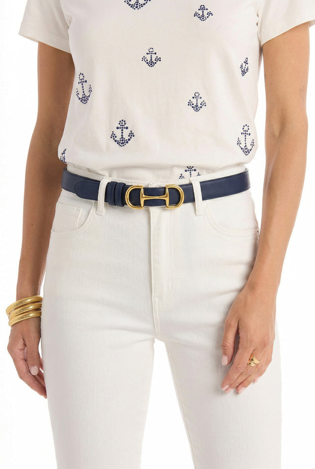 A person wearing a white t-shirt with blue anchors, white jeans, and the Bettie Belt - Navy with a gold buckle, complemented by several gold bangles and a gold ring. The image is cropped from the shoulders to the thighs.