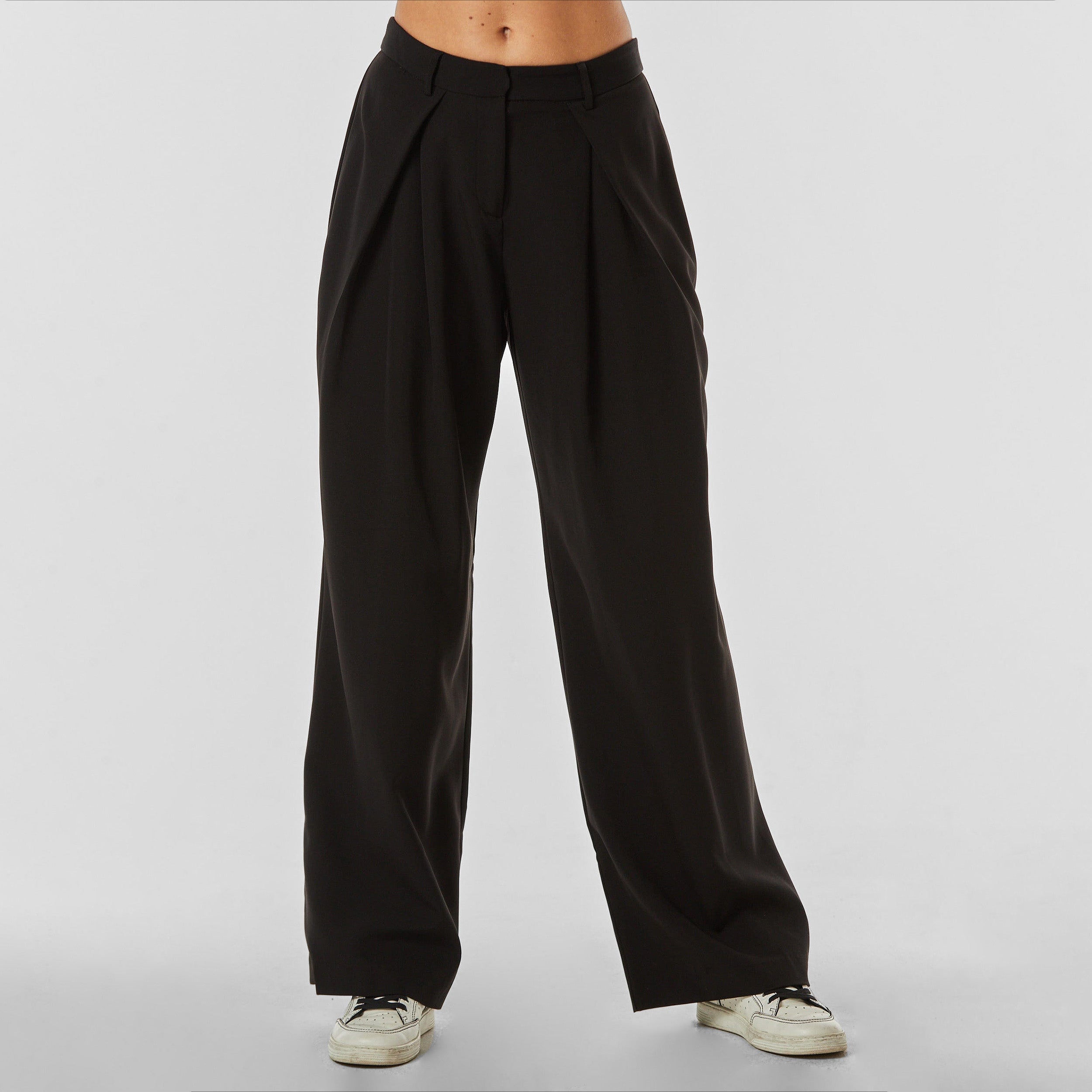 Front view of woman wearing pleated black trousers with stretch fabric