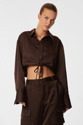 A person is wearing the Milan Satin Button Up in Espresso, a dark brown long-sleeve satin shirt with a drawstring tie-waist, paired with matching high-waisted cargo pants featuring subtle cargo detailing. Their hair is styled in a high bun, and they stand against a plain white background.