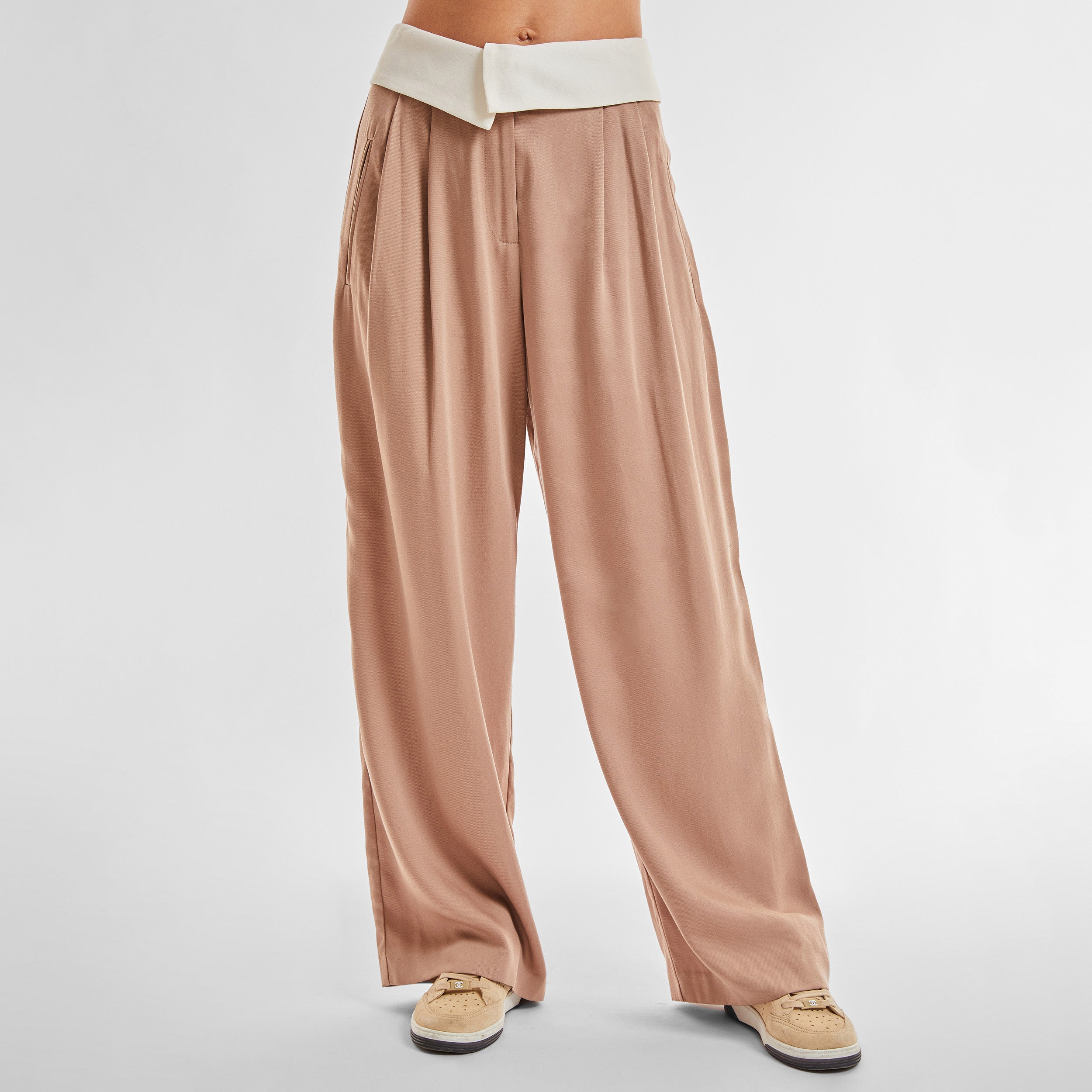 Front view of woman wearing light brown trousers with white foldover waistband detail.