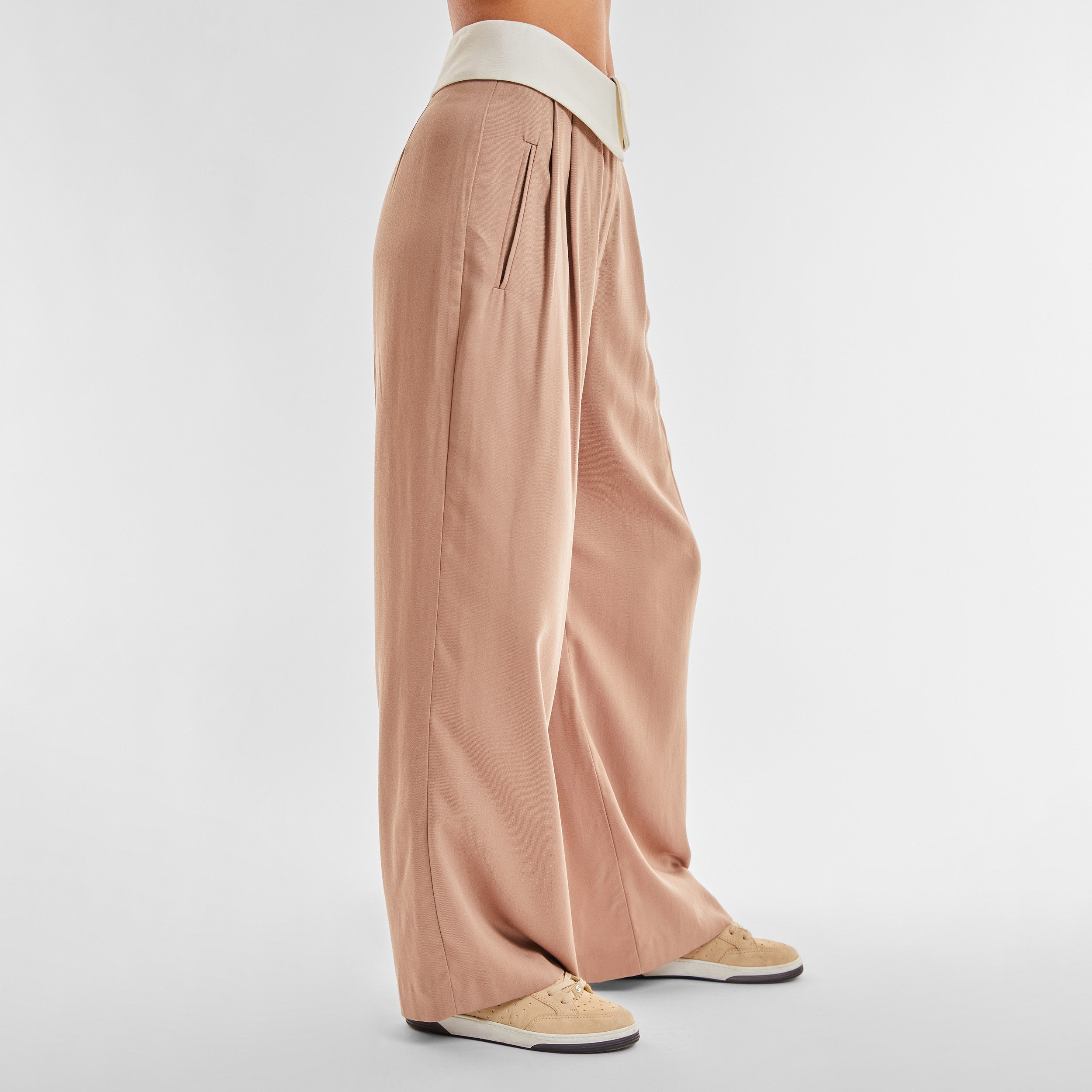 Side view of woman wearing light brown trousers with white foldover waistband detail.