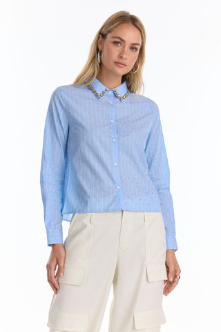 A woman wears the Josefina Crystal Button Up - Blue Stripe (Preorder), a light blue striped blouse with a crystal-encrusted collar, paired with white cargo-style pants, standing against a plain white background.