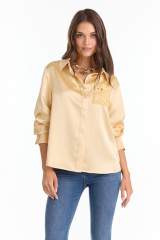 A woman with long brown hair wears the Amelia Silky Lace Blouse - Butter Yellow (Preorder), featuring a relaxed fit and lace chest pocket detail. She pairs it with blue jeans, standing against a white background and smiling at the camera.