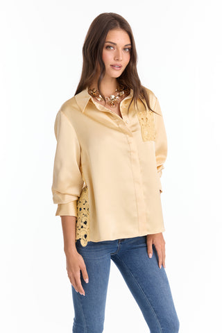 A woman wears the Amelia Silky Lace Blouse in butter yellow, featuring a relaxed fit and lace details on the back and chest. She pairs it with blue jeans, accessorized with a statement necklace, against a white background.