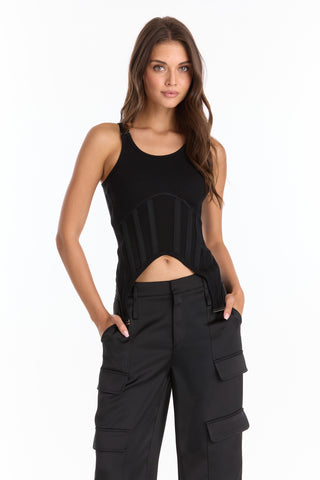 A woman with long brown hair stands against a white background, hands in her pockets, wearing the Kiara Garter Tank - Black and black cargo pants.