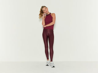 Two women stand confidently in athletic wear against a neutral background. One wears a burgundy set with a matching jacket, the other in a black set with a matching jacket draped over her shoulders.