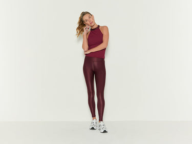 Two women stand confidently in athletic wear against a neutral background. One wears a burgundy set with a matching jacket, the other in a black set with a matching jacket draped over her shoulders.