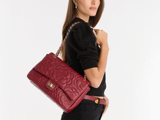 A person with manicured nails holding a stylish, small handbag with metallic circular embellishments and a silver handle against a black background. The handbag has a drawstring closure with dangling metal accents.