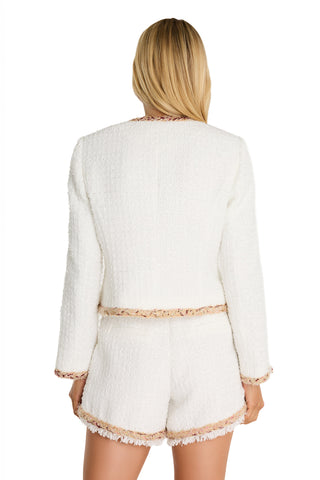 A woman with long blonde hair, seen from behind, wears a textured Joane Tweed Jacket - Pearl Multi with pearl statement buttons and matching white shorts with frayed edges and subtle beige trim.