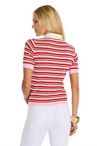 A woman with long blonde hair, seen from the back against a white background, wears the Leya Polo Shirt - Summer Multi with gold embossed buttons and white pants.