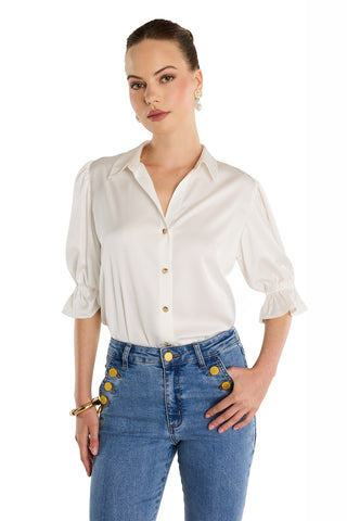 A woman stands against a white background wearing the Cindy Ruffle Sleeve Blouse in white, styled with high-waisted blue jeans. Her hair is pulled back, and she accessorizes with gold earrings and a bracelet.