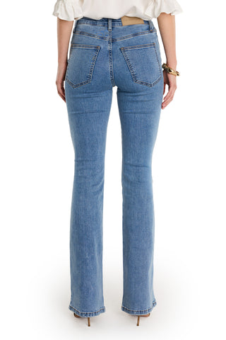 A person is shown from the back wearing the high-waisted Allegra Bootcut Jean - Medium Blue with visible back pockets, subtle ankle flare, and gold detailing, paired with a white shirt, heels, and a bracelet.