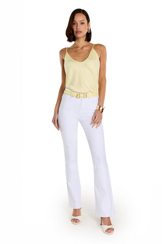 A woman stands against a white background wearing the Yara Silk Camisole in Sunshine Yellow, paired with white flared pants, a matching belt, heeled sandals, gold hoop earrings, and a gold bracelet.