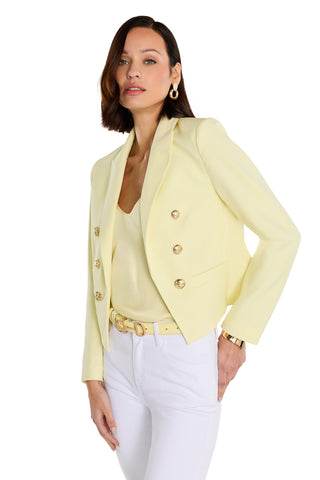 A woman poses with one hand on her hip against a white background, wearing the Gabrielle Double Breasted Blazer in Sunshine Yellow, a matching top, white pants, gold-buckled belt, gold hoop earrings, and a gold watch.