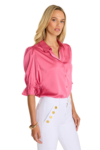 A woman models the Cindy Ruffle Sleeve Blouse in Petal Pink with puffed sleeves and white high-waisted pants with gold buttons, posing against a plain white background.