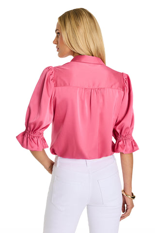 A woman with long blonde hair is wearing the Cindy Ruffle Sleeve Blouse in Petal Pink, paired with white pants. She stands with her back to the camera against a white background.