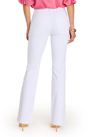 Someone is shown from the back wearing the Allegra Bootcut Jean - White with gold detailing, paired with a pink puff-sleeve top, nude heels, and a gold bracelet.