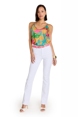 A woman faces forward, wearing the Yara Silk Camisole - Dolce Sun with adjustable straps— a vibrant, silky piece—styled with white pants, a pink belt, sandals, gold bangle, and straight hair. She stands confidently against a plain white background.