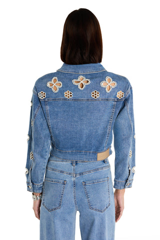 A person is shown from the back wearing the Kaia Pearl Jean Jacket in Medium Blue, featuring floral cutouts on the back and sleeves, paired with matching high-waisted jeans against a white background.