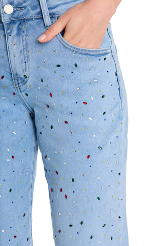 A person wearing the Ren Cropped Cuff Jean - Confetti, light blue cropped denim with four-way stretch and rainbow gem details, one hand in the front pocket.