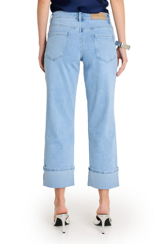 A woman is seen from behind wearing the Ren Cropped Cuff Jean - Confetti, featuring light blue four-way stretch denim, large cuffs, and back pockets, paired with white heels to showcase the jeans' unique back details.