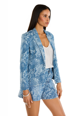 A woman with long, straight brown hair and minimal jewelry wears the Marie Single Breasted Blazer - Crystal Snake with matching shorts and a white top, standing against a plain white background.