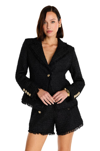 A woman with shoulder-length brown hair wears the Giselle Single Breasted Tweed Blazer - Black with gold buttons and matching black shorts, standing forward with hands clasped at her waist against a white background.