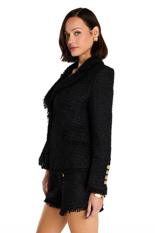 Woman with short brown hair wears the black Giselle Single Breasted Tweed Blazer, featuring gold buttons, paired with matching black shorts. She stands against a white background, looking slightly over her shoulder.