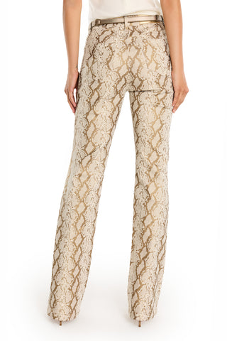 A person wearing the Aria Flare Jean - Gold Python, featuring a beige and brown snake print with a slim bootcut silhouette, is seen from the back and paired with a light-colored top.