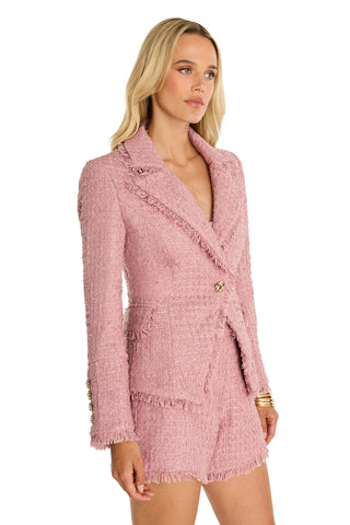 A woman with long blonde hair stands against a white background wearing the Giselle Single Breasted Tweed Blazer in blush, featuring textured pink tweed, gold button details, frayed edges, and a tailored fit with matching shorts.