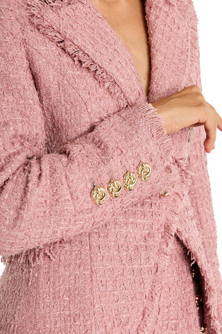 A close-up of a person wearing the Giselle Single Breasted Tweed Blazer - Blush, featuring textured pink tweed, gold decorative cuff buttons, frayed edges, and a bent elbow.