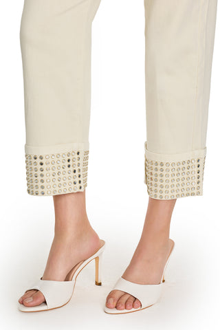 A person wears the Ren Cropped Cuff Jean - Gold Mirror with metallic-studded cuffs and open-toe, high-heeled cream mules against a white background.