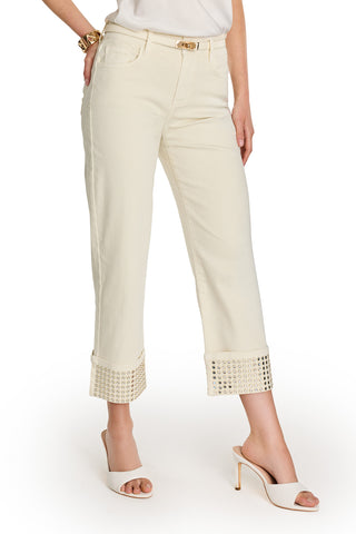 A woman wears the Ren Cropped Cuff Jean - Gold Mirror with white heeled mules and a white top. One hand is in her pocket, the other by her side, showcasing a gold bracelet.