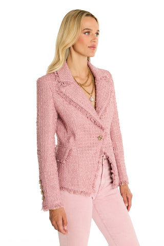 A woman with long blonde hair wears the Giselle Single Breasted Tweed Blazer in blush, styled with matching pants and layered gold necklaces. She stands at an angle against a white background, looking to the side.
