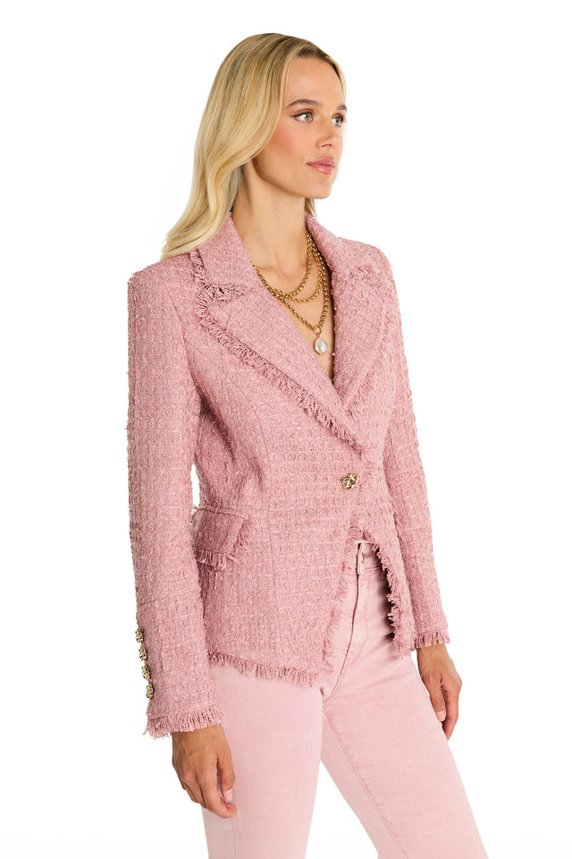 A woman with long blonde hair wears the Giselle Single Breasted Tweed Blazer in blush, styled with matching pants and layered gold necklaces. She stands at an angle against a white background, looking to the side.