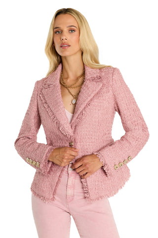 A woman with long blonde hair wears the Giselle Single Breasted Tweed Blazer in blush, styled with layered necklaces and matching pink pants. She stands facing forward, adjusting her jacket.