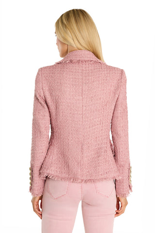 A woman with long blonde hair is seen from the back wearing the Giselle Single Breasted Tweed Blazer in blush, featuring frayed edges and gold sleeve buttons, paired with light pink jeans against a white background.