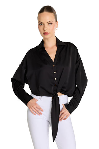 A woman stands with hands on hips against a white background, wearing the Cecilia Silk Tie-Front Blouse in black with long sleeves and white pants.