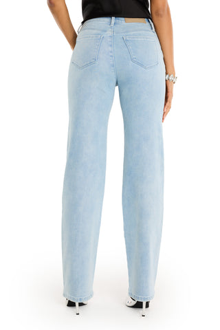 A person stands upright, shown from the back, wearing the Tara Crystal Jean - Light Blue (high-rise, wide-leg), a black top, and white open-toe heeled shoes.