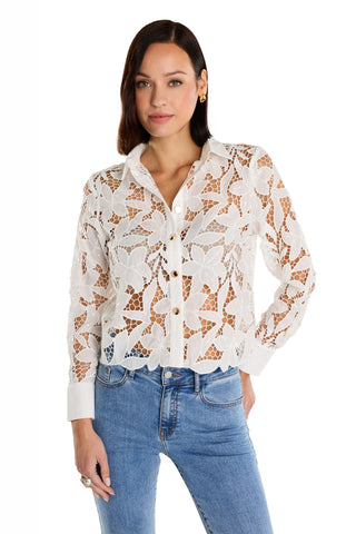 A woman models the Mina Lace Blouse in white, featuring a sheer, delicate floral lace design, paired with blue jeans and posing with one hand in her pocket against a white background.