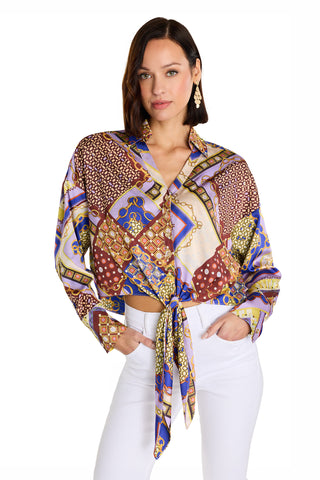 Woman with shoulder-length dark hair wears the Cecilia Silk Tie-Front Blouse in Riviera Chain, paired with white pants and gold earrings, standing with one hand in her pocket against a white background.