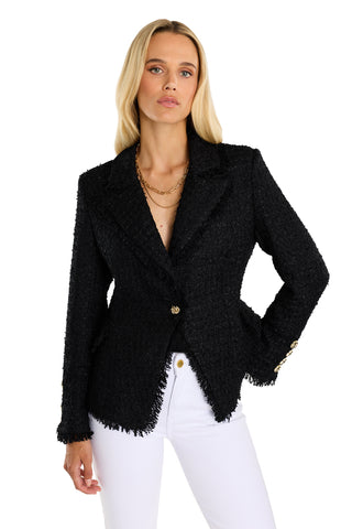A woman with long blonde hair wears the Giselle Single Breasted Tweed Blazer - Black, styled with white pants. She stands against a plain white background, posing with one hand on her hip.