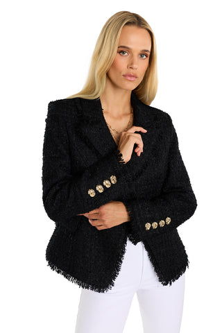 A woman with long blonde hair wears the Giselle Single Breasted Tweed Blazer in black with gold buttons and white pants, standing against a white background.