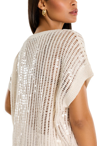 A woman with straight brown hair wears the Carmela Sequin Knit Top in pearl and a gold earring, showing her back and profile against a white background.