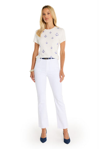 A woman with long blonde hair wears the Amaya Ultra Soft T-Shirt – Crystal Anchors, featuring small blue anchor prints, styled with white pants and blue heels, standing against a white background.
